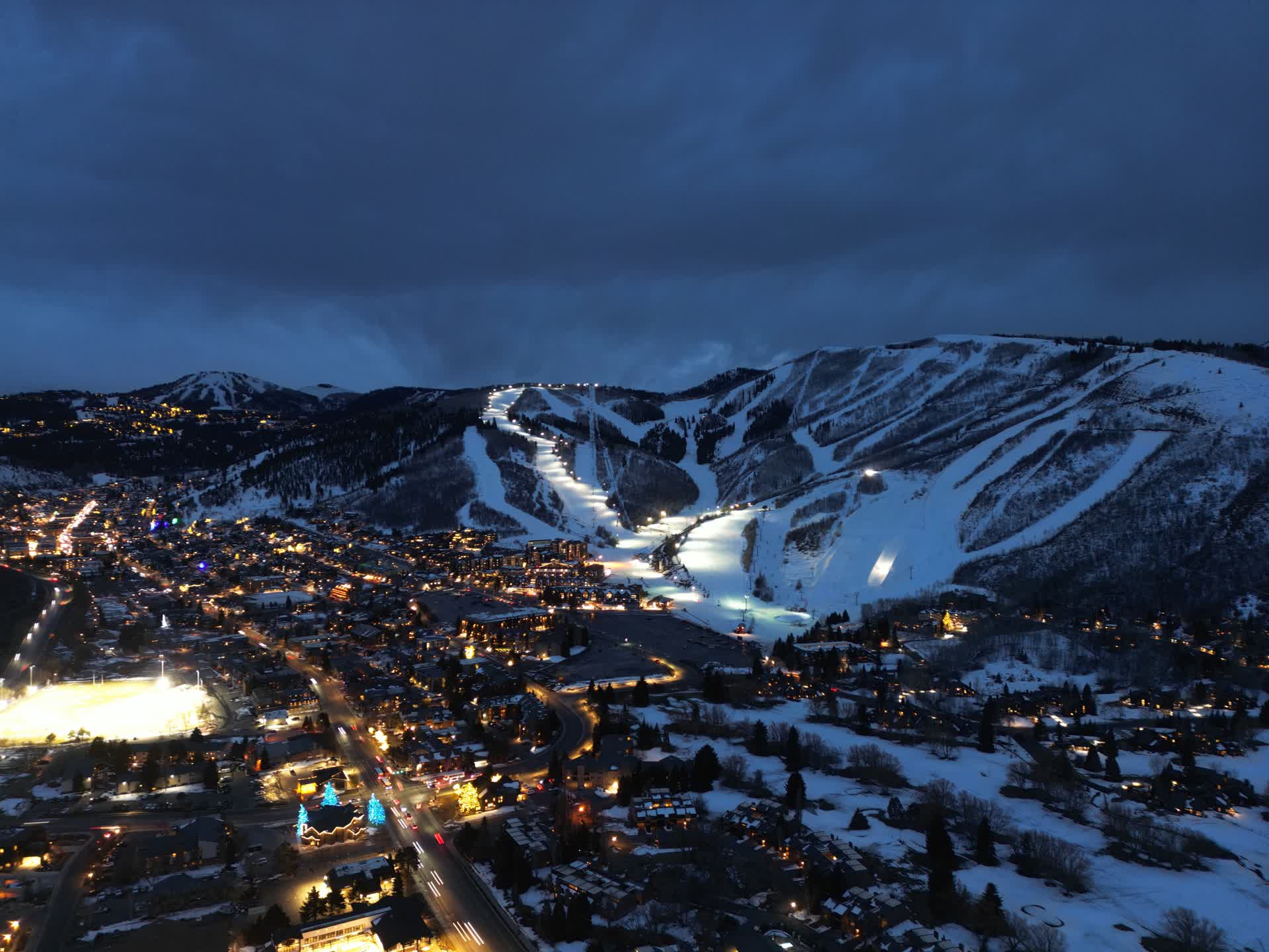 Aerial drone view of ski resort at night with lit runs and town below